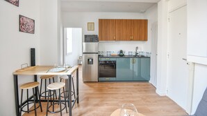 A modern kitchen with wooden cabinets, a stainless steel refrigerator, and a bar area with stools. - Coeur Endoume - Bel appart 1 ch proche Vieux Port (Marseille)