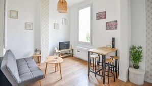 A modern living room with a sofa, a dining table with stools, a TV, and a potted plant. - Coeur Endoume - Bel appart 1 ch proche Vieux Port (Marseille)