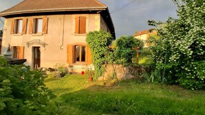 A two-story house with a sloped roof, a front door, and a small garden area with plants and a bench. - Vacation home near the lake, ideal for families (Montferrat)