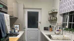 A compact kitchen with a washing machine, a sink, and a door with a frosted glass panel. - The Bungalow Birmingham NEC Airport Bullring (Birmingham)
