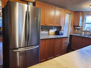 A kitchen with wooden cabinets, a stainless steel refrigerator, a toaster, and a window. - SHADY DECK LODGE, TURKEY POINT, July & August min 7 days SAT. to SAT. $2000.00+ (Vittoria)