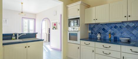 Una cocina con armarios blancos, encimera azul y microondas.