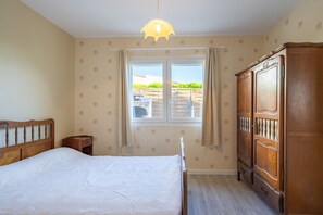 Een slaapkamer met een bed, een kledingkast, een raam met gordijnen en een hanglamp.