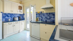 A kitchen with white cabinets, blue tiles, a dishwasher, and a sink. - Holiday Home “Quartier Calme” with Private Garden (Royan)
