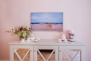 Ein weißes Schranks mit einem Gemälde einer Strandansicht, einer Blumenvase und einem rosafarbenen Tee-Set.