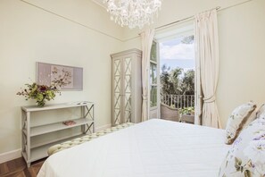 Een slaapkamer met een bed, een kaptafel, een kroonluchter en uitzicht op het omliggende landschap.