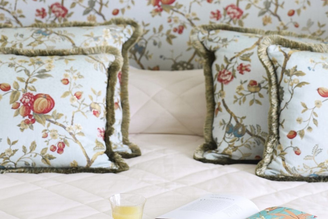 Ein Bett mit einer gesteppten Decke, zwei Kissen mit Blumenmuster und ein Glas Wasser darauf.