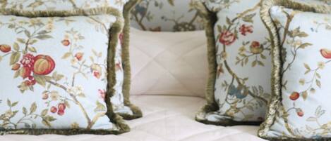 Uma cama com cobertura acolchoada, dois travesseiros com estampas florais e um copo de água sobre a cama.