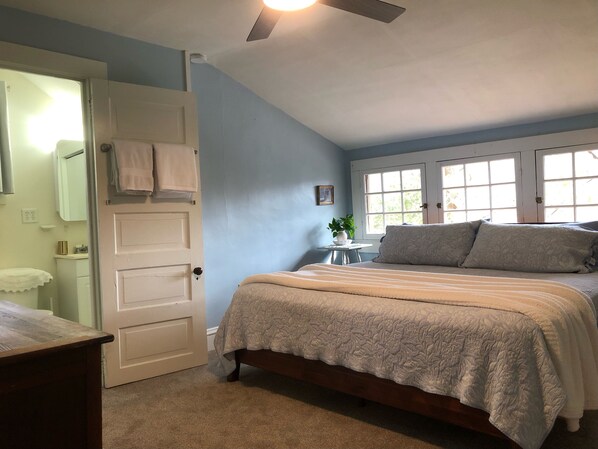 A bedroom with a bed, a door, a small table with a plant, and a window.