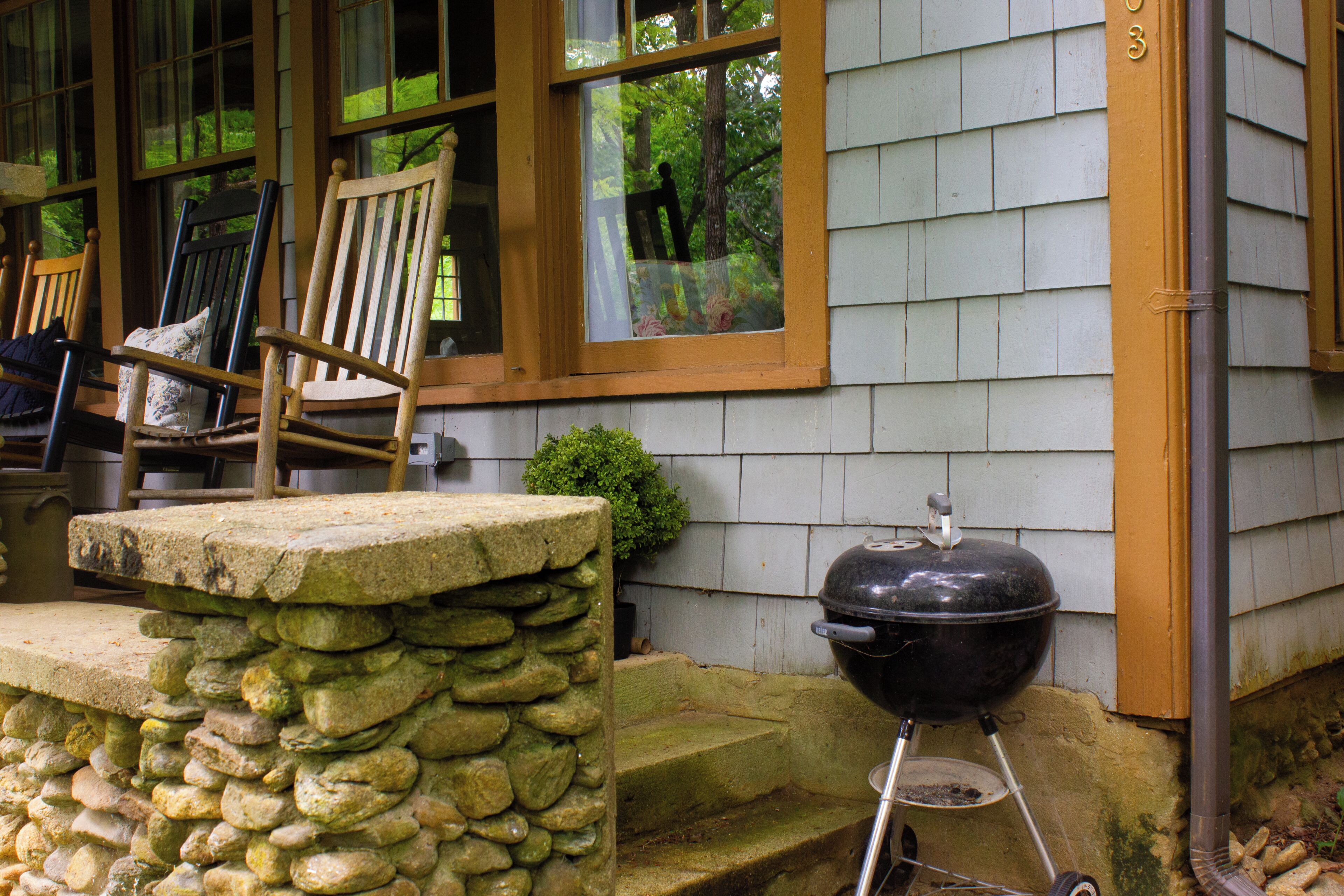 A stone ledge, a wooden chair, and a barbecue grill outside a house.