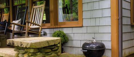 A stone ledge, a wooden chair, and a barbecue grill outside a house.