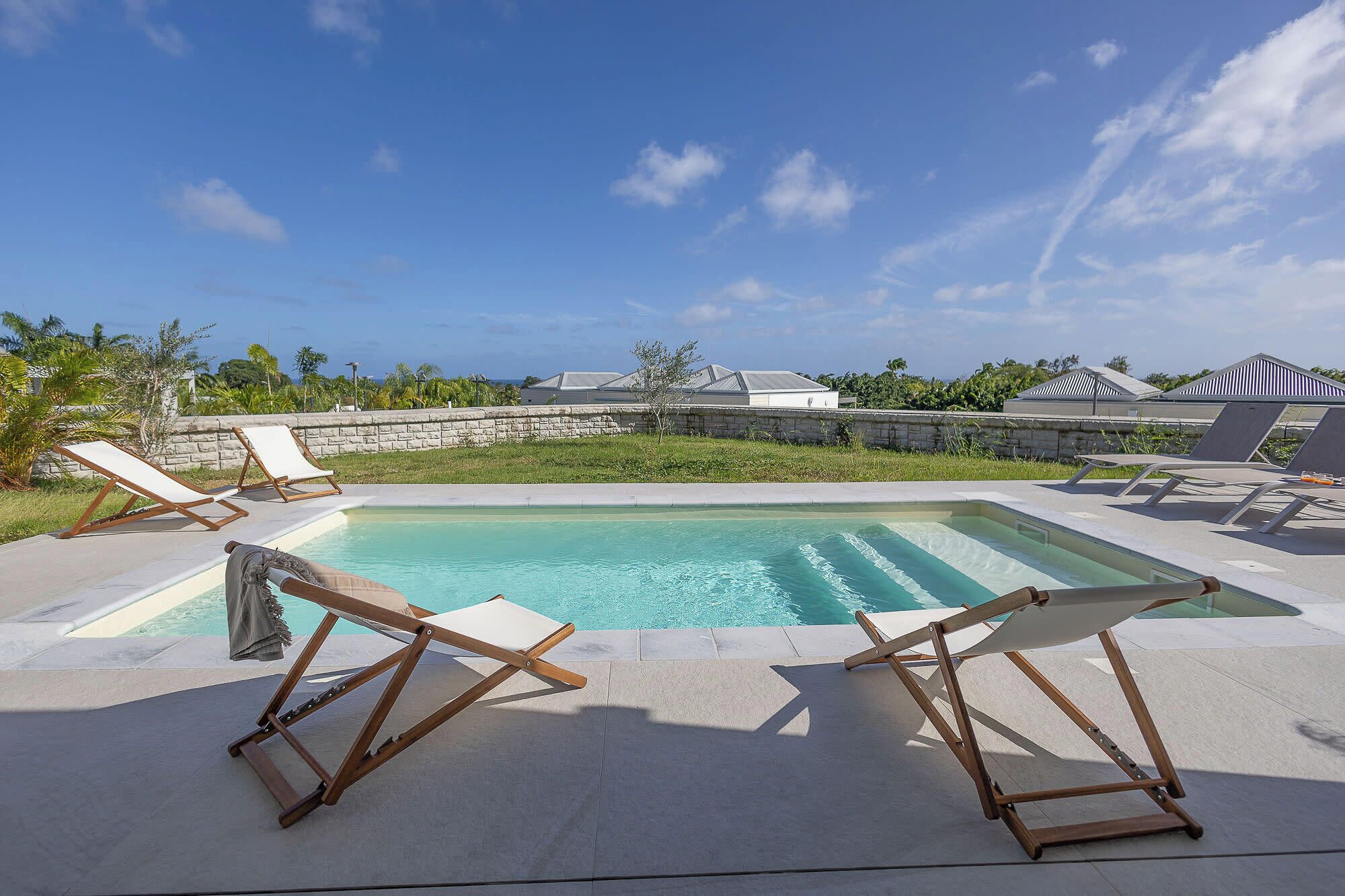 Une piscine avec des chaises longues, un mur en pierre et des bâtiments en arrière-plan.