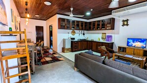 A living room with a sofa, a wooden ladder, a kitchen with wooden cabinets, a television, and a ceiling fan. - Kay's Place Train House Jambo (Zanzibar Town)