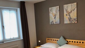 A neatly made double bed with white linens, a wooden headboard, and two wall-mounted paintings of deer. - 2_9 Cosy Kaprun Apartment by Interhome (Kaprun)