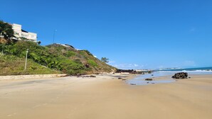 Ein Strand mit einem Gebäude auf einem Hügel, bewölkter Himmel und Meereswellen.