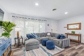 Ein modernes Wohnzimmer mit einem Ecksofa, Poufs, einem Couchtisch und einer Anrichte.