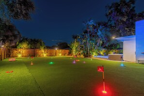 Ein Garten mit Kunstrasen, einem Putting-Green und einem kleinen Poolbereich.