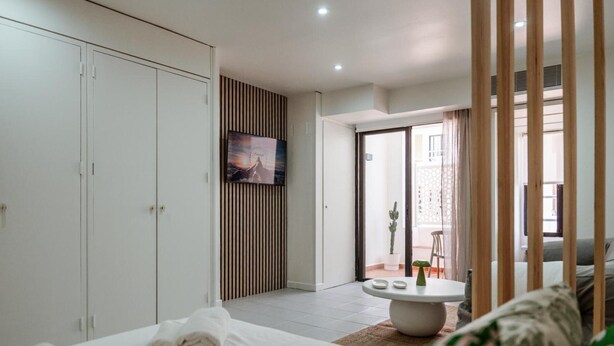 Une chambre d’hôtel moderne équipée d’un lit, d’une télévision, d’un coin repas et d’une porte-fenêtre coulissante donnant sur un balcon.