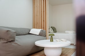 A modern room with a grey sofa, a round white table with a green object, and a bed with white linens.