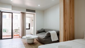 Une chambre moderne avec un lit, un canapé, une table basse ronde et une porte-fenêtre coulissante donnant sur un balcon.