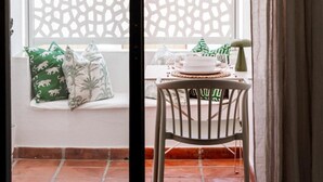 Une pièce dotée d’une porte-fenêtre coulissante donnant sur un balcon, d’une petite table avec une chaise et d’un paravent décoratif.