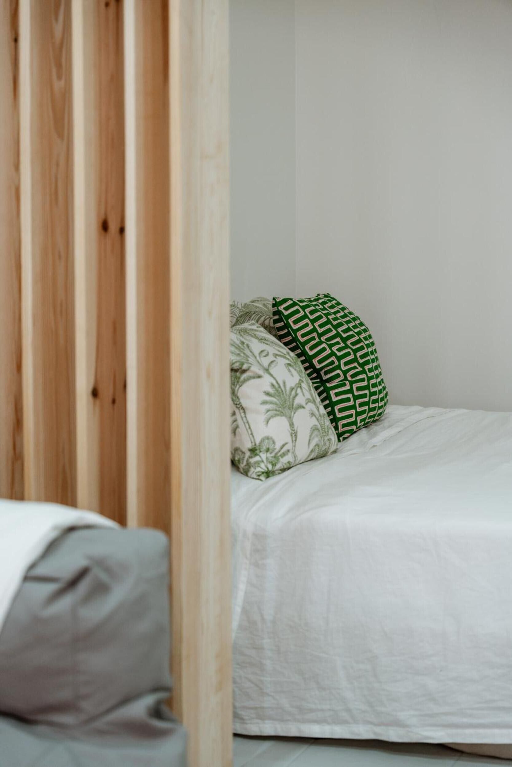 Una cama con ropa de cama blanca y dos almohadas, una con estampado verde y otra con diseño de hoja de palmera.