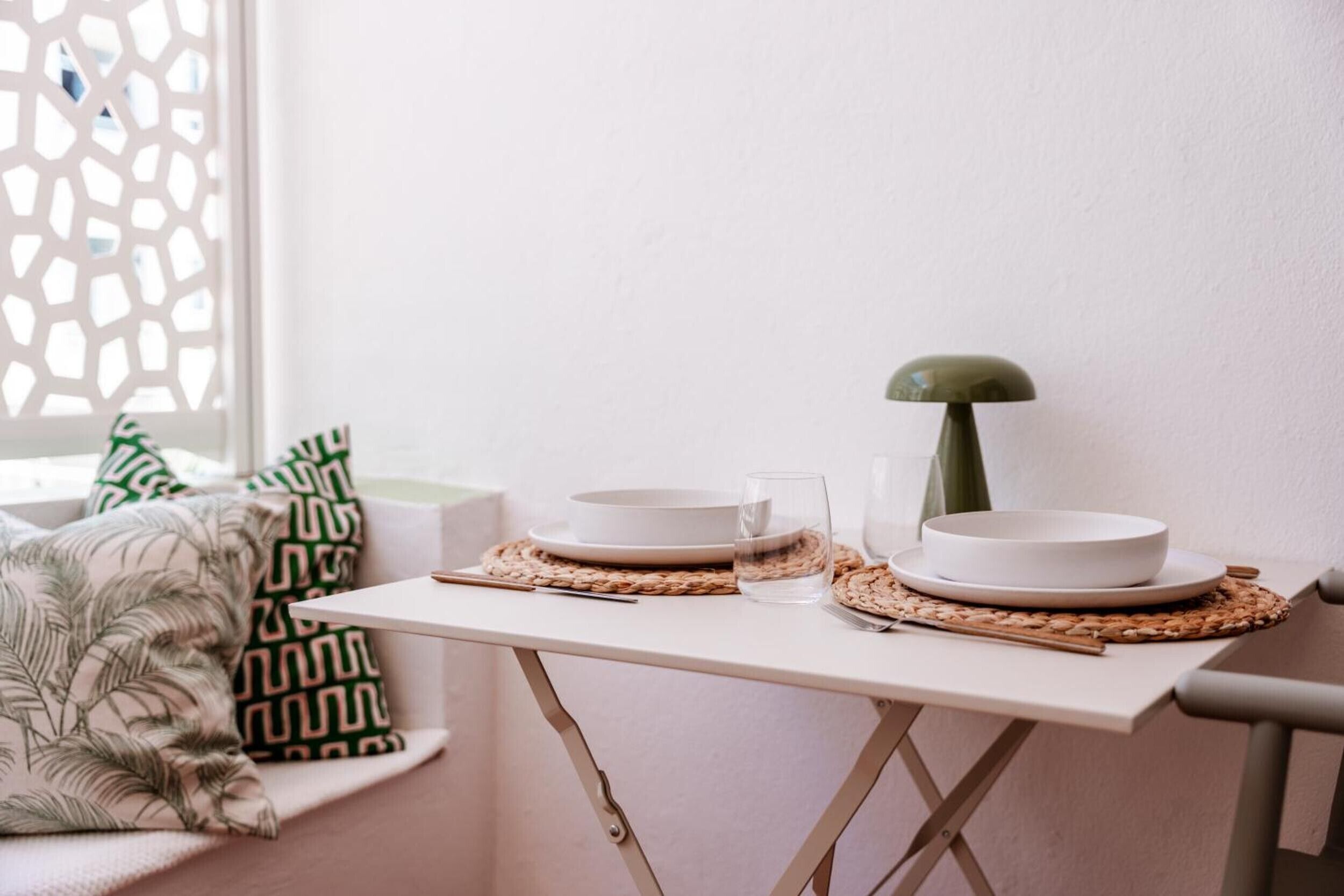 A table with two white plates, a glass, and a green lamp.