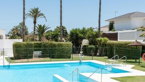 Une piscine à l’eau d’un bleu cristallin, entourée de palmiers et bordée d’une haie bien entretenue.