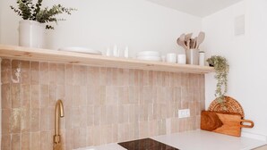 Une cuisine avec un plan de travail blanc, un crédence carrelé de couleur beige, un robinet doré et une planche à découper en bois.