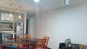 Kompakti oleskelutila, jossa on ruokailualue, sohva, tuuletin ja pieni keittiö.