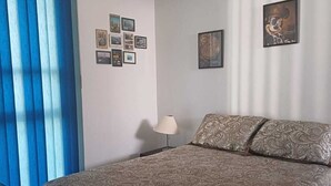 Makuuhuoneessa on sänky, yöpöytä, lamppu, seinä, jossa on kuvia, ja siniset verhot.
