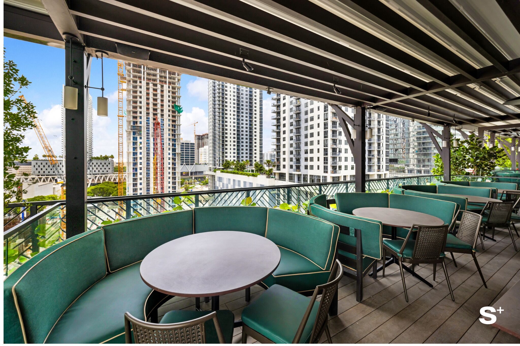 A rooftop terrace with green seating, a round table, and a view of high-rise buildings.