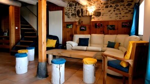A cozy living room with a stone wall, wooden beams, a sofa, a chair, and ottomans.