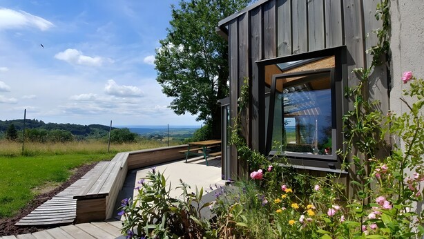 A modern building with a large window, a wooden deck, and a garden with flowers.