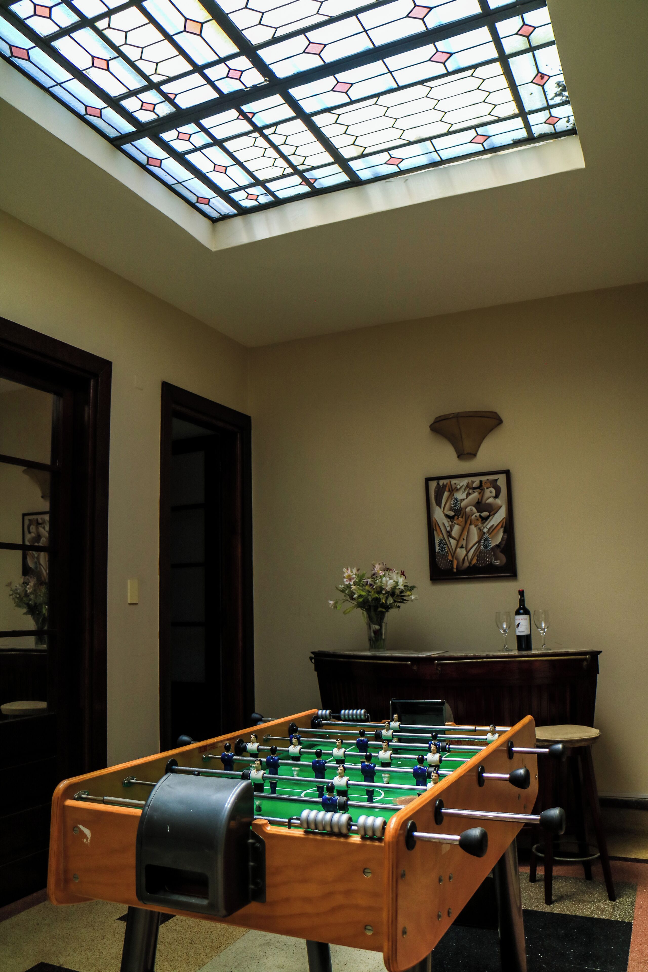 A foosball table in a room with a skylight, a painting on the wall, and a bar area.