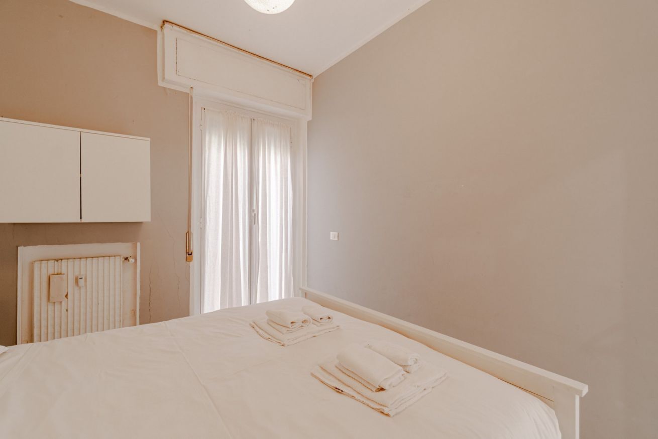 A bedroom with a bed, a radiator, a wardrobe, and a window with curtains.