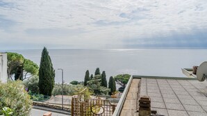 Vista al mar des d'una terrassa al terrat, amb cel serè, mar tranquil i una riba llunyana.
