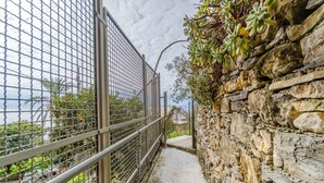 Un camí estret delimitat per una tanca metàl·lica i un mur de pedra, que condueix a una vista del mar.