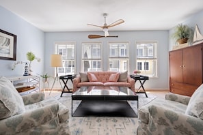 A living room with a sofa, two armchairs, a coffee table, a ceiling fan, and large windows.