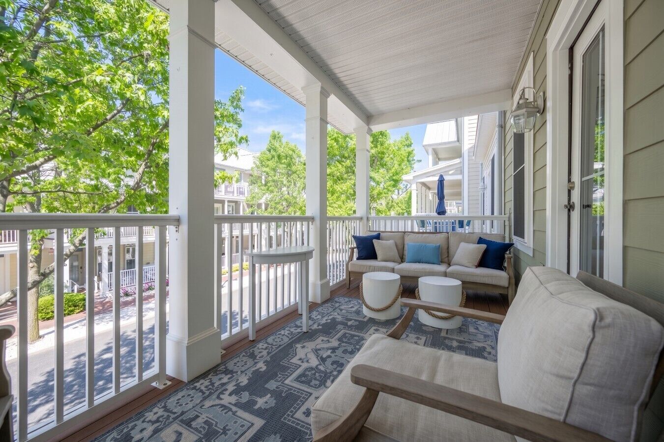 A covered porch with a sofa, two side tables, and a patterned rug.