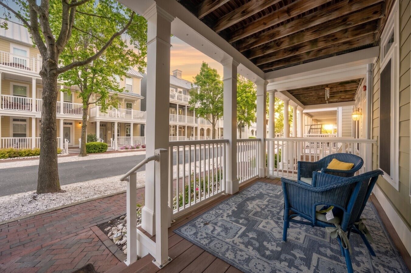 A covered porch with a seating area, white railings, and a view of neighboring buildings.