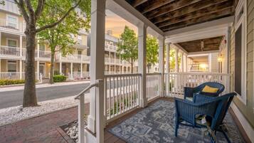 A covered porch with a seating area, white railings, and a view of neighboring buildings.