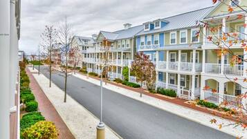 A row of multi-story residential buildings with balconies, a paved street, and a sidewalk with trimmed bushes.