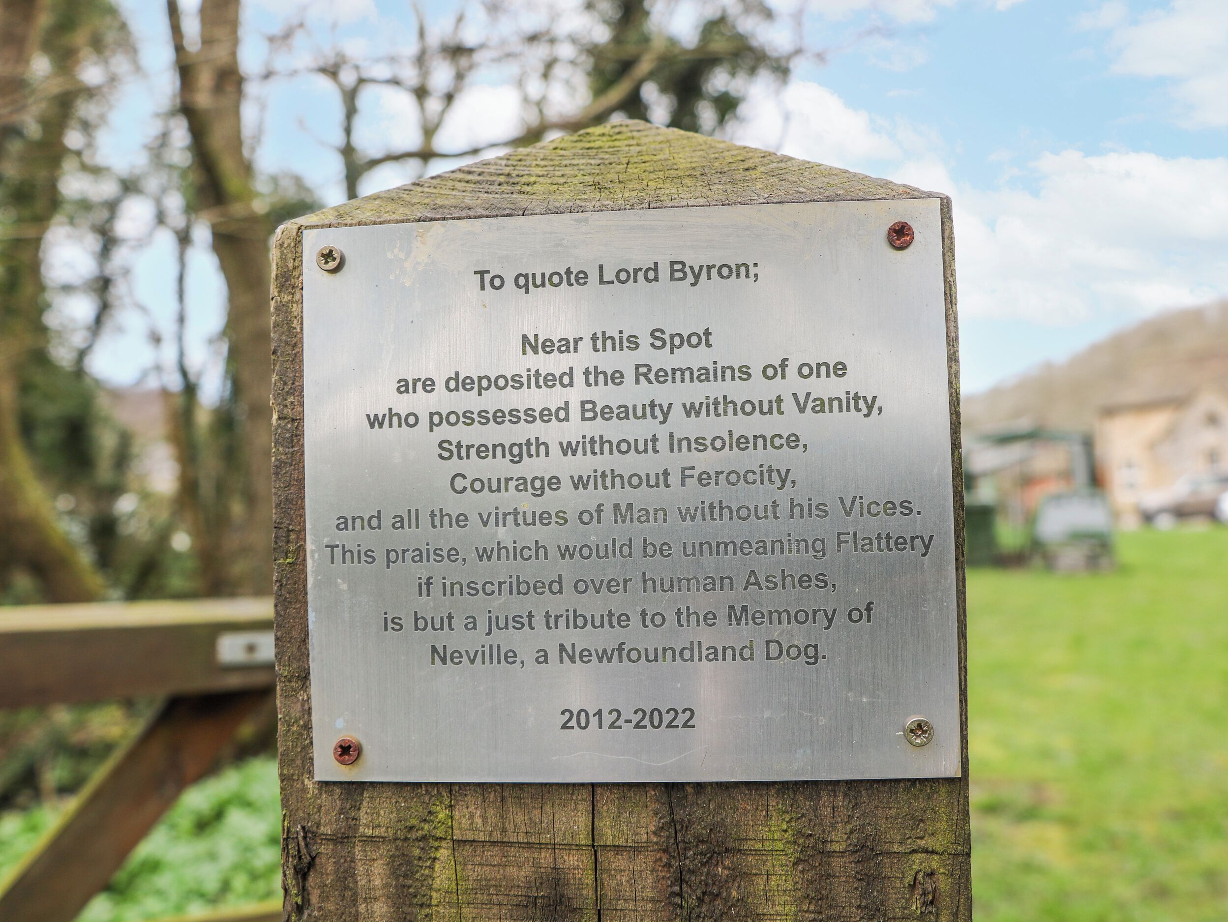 A memorial plaque on a wooden post with engraved text.
