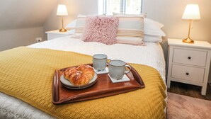 A neatly made bed with a yellow blanket, two bedside lamps, a fluffy pink pillow, and a tray with a croissant, a mug, and a cup. - Little Mill (Chesterfield)