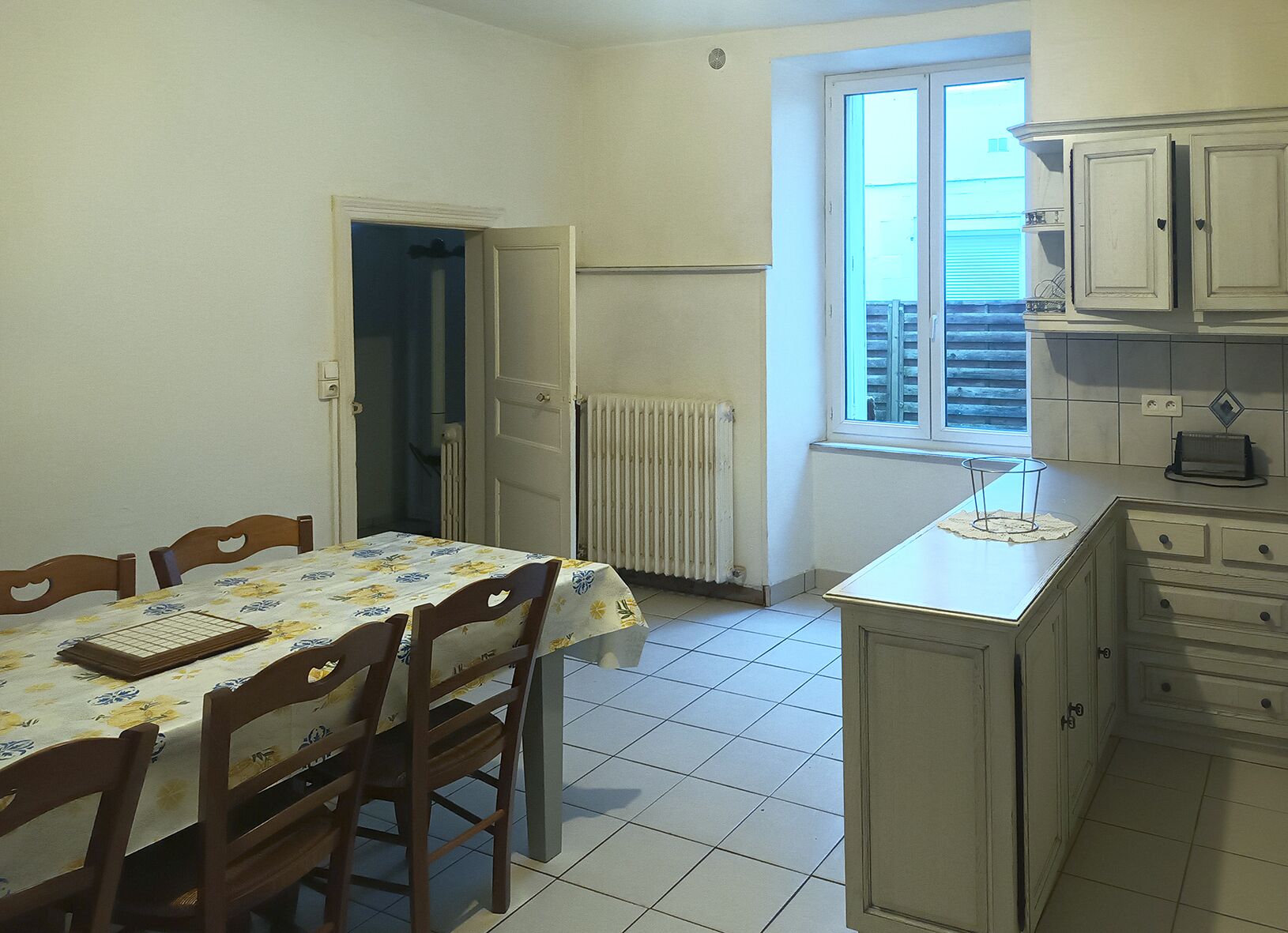A room with a dining table, chairs, a window, a radiator, and cabinets.