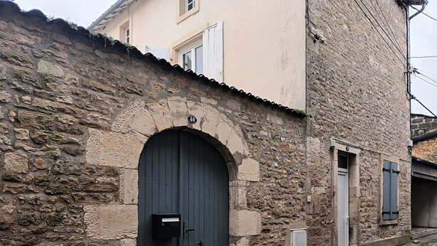 Ein Steinhaus mit einer dunklen Rundbogenöffnung, einem Briefkasten und einem kleinen Fenster.