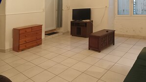 Ein Zimmer mit Fliesenboden, einem Holzschrank, einem Fernseher auf einem Schrank und einem grünen Sofa.