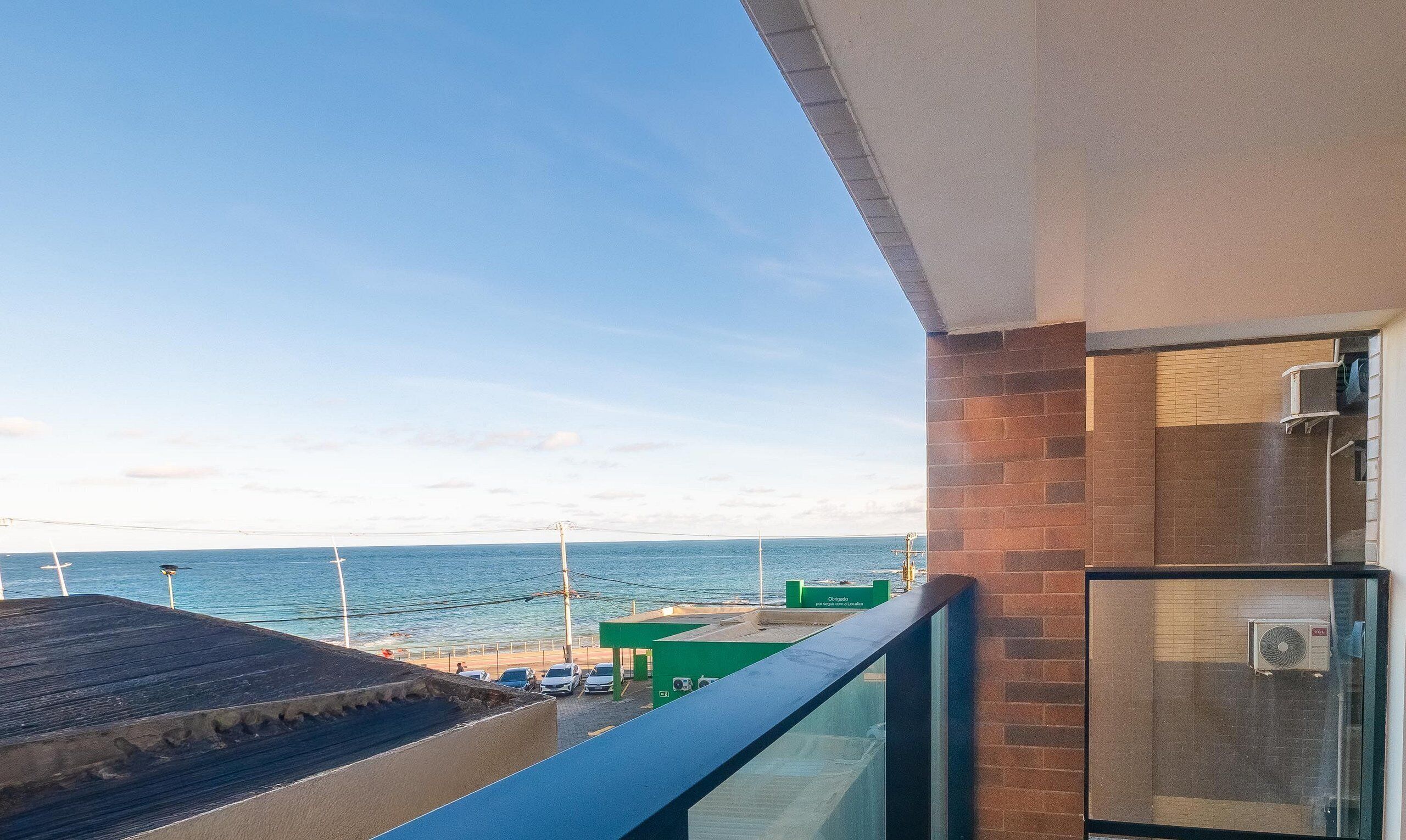 Un balcón con vistas al mar, un edificio verde y un muro de ladrillo.