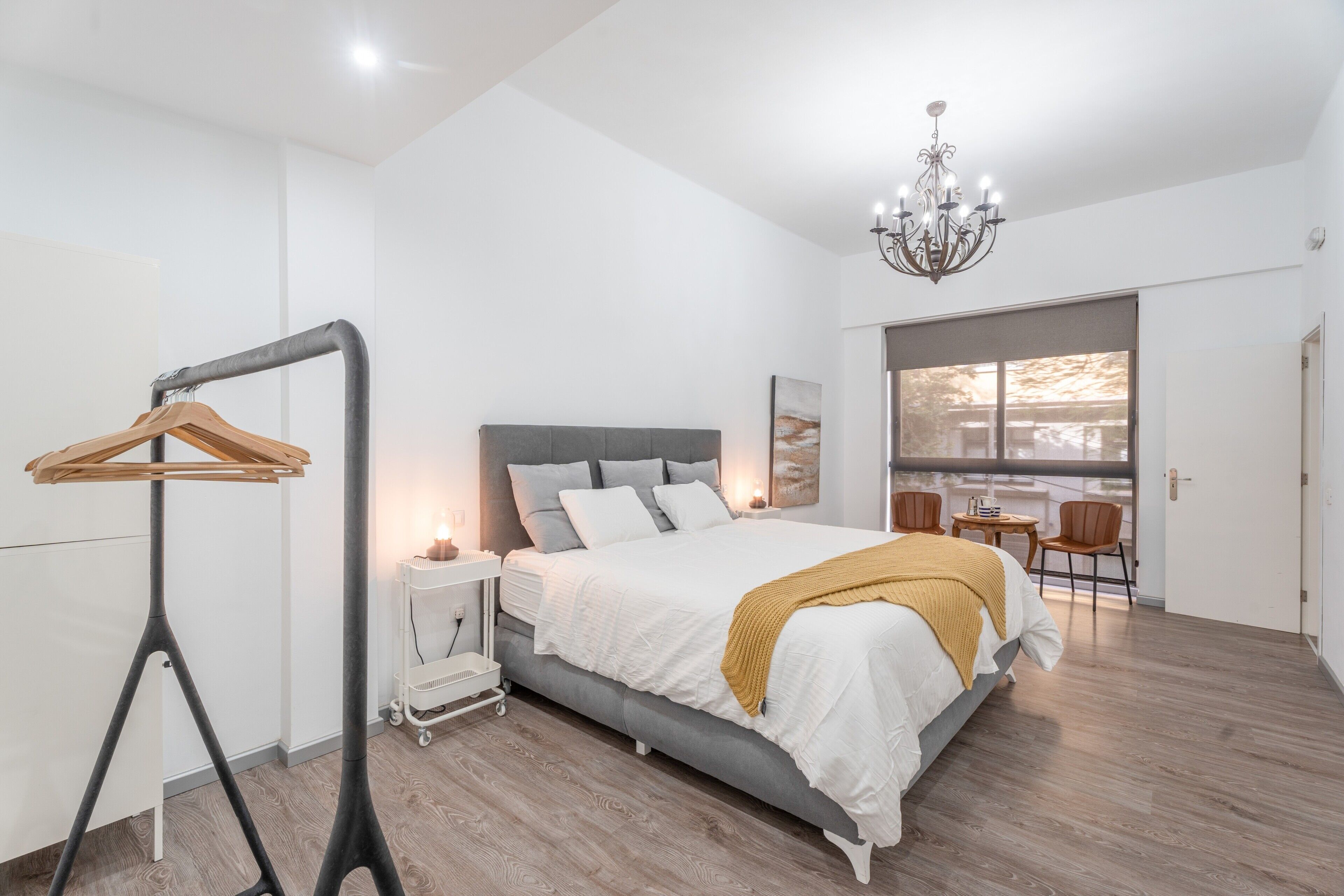 A bedroom with a bed, bedside table, lamp, and a view of the outdoors.